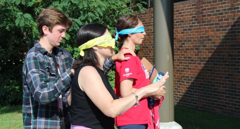 A young person guides two blindfolded people by the shoulders at the family seminar of an outward bound intercept course 